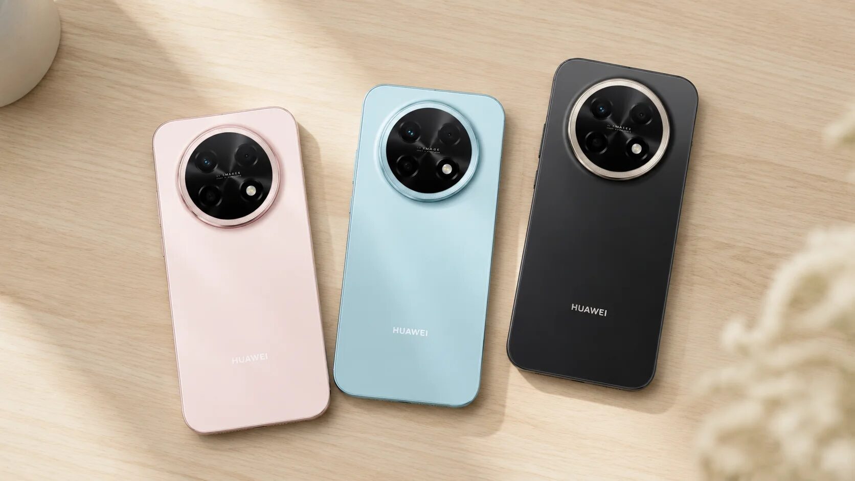 Три смартфона HUAWEI nova 15 Max в розовом, голубом и черном цветах лежат на столе задними крышками вверх